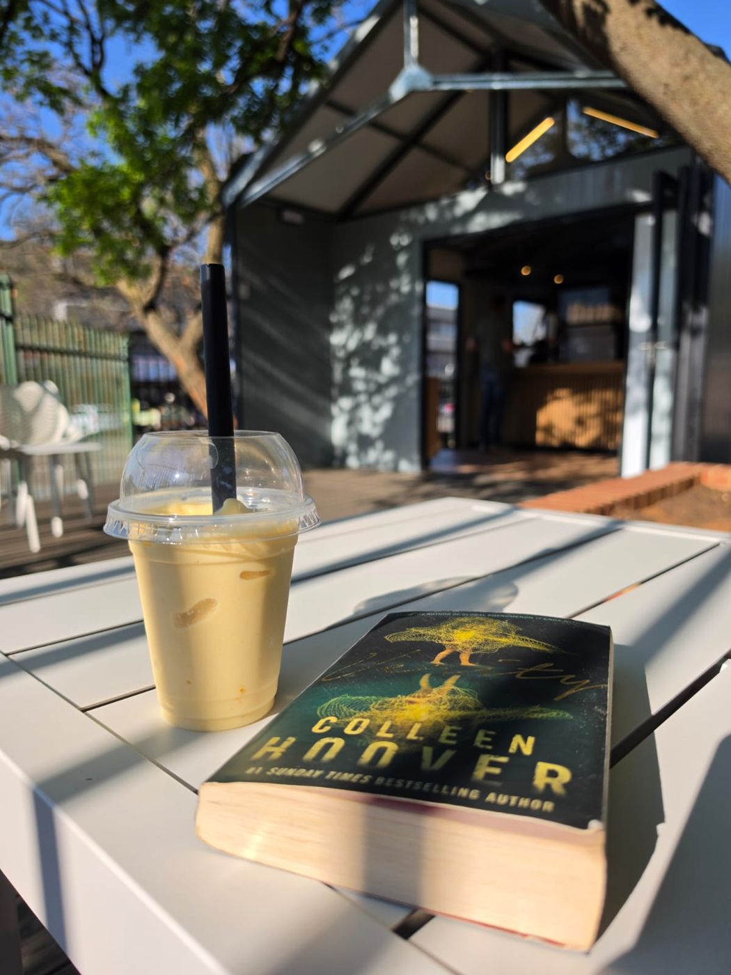 Iced coffee and a book on a table outside Tiny Town Café